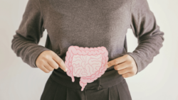 A person holds a paper illustration of the digestive tract against their abdomen.