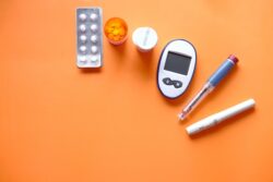 Diabetes care items, including tablets, a pill bottle, a glucose meter, and injection pens, arranged on an orange background.