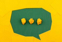 A green speech‑bubble shape with three crumpled yellow paper balls inside, surrounded by yellow notepaper.