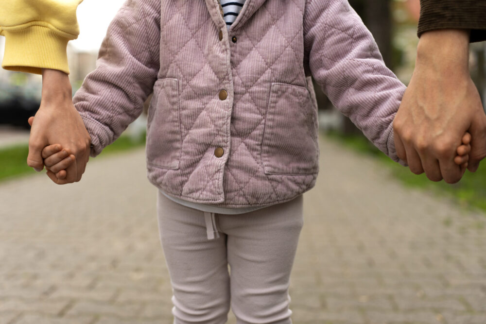 A child stands on a path holding hands with two adults on either side.