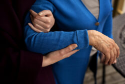 An arm is gently supported by another person while walking outdoors.