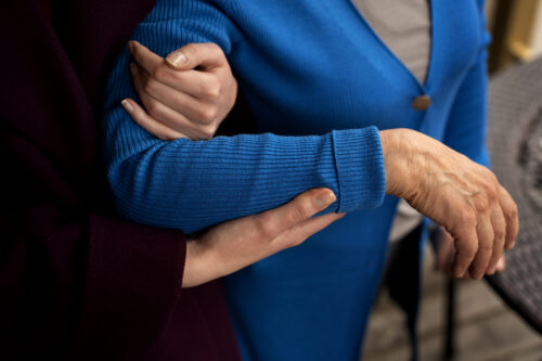 An arm is gently supported by another person while walking outdoors.