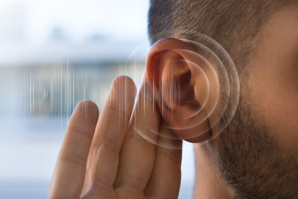 A person holds a hand to the ear with a circular soundwave graphic beside it.
