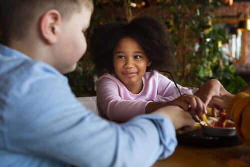 Children sit together at a table sharing food and drinks in a restaurant setting.