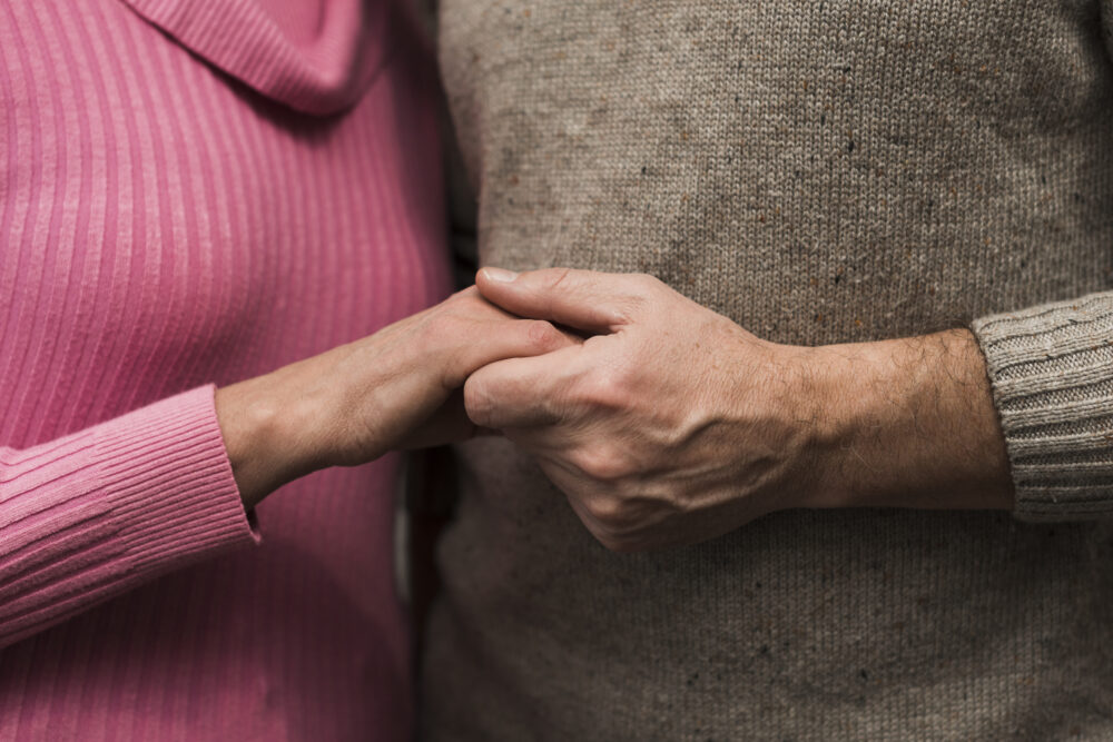 The two people are standing close together, facing one another slightly, with their hands gently clasped between them.