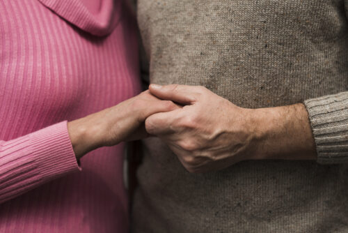 The two people are standing close together, facing one another slightly, with their hands gently clasped between them.