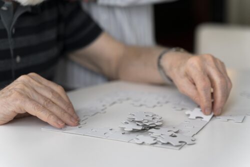 Hands working on a light‑coloured jigsaw puzzle on a table, suggesting a calming, cognitive‑support activity.