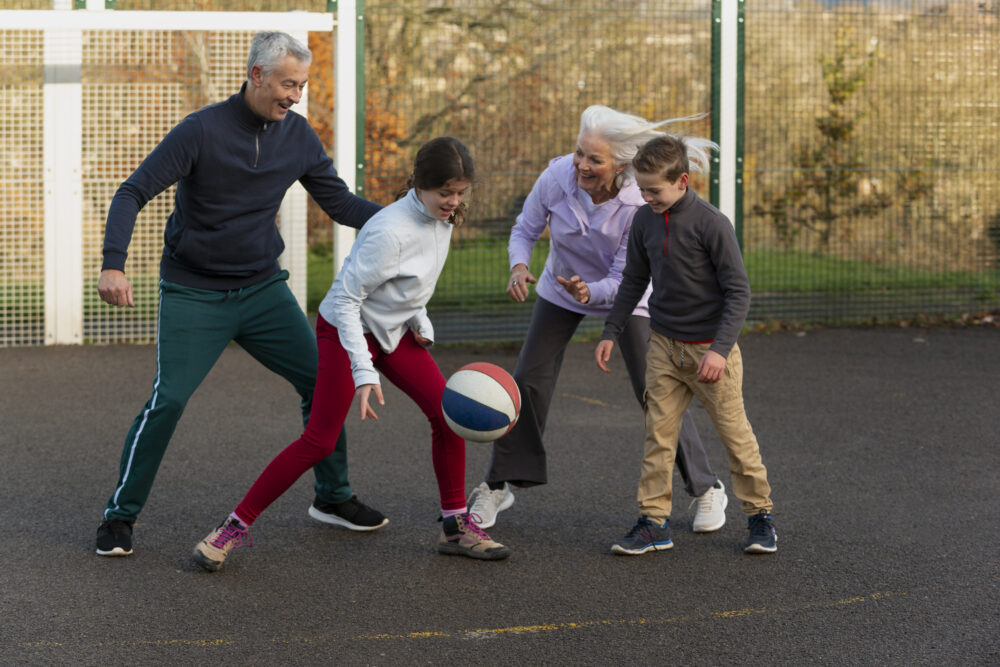 A group of people of different ages play basketball together on an outdoor court.