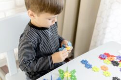 A child sits at a table assembling colourful interlocking plastic pieces.
