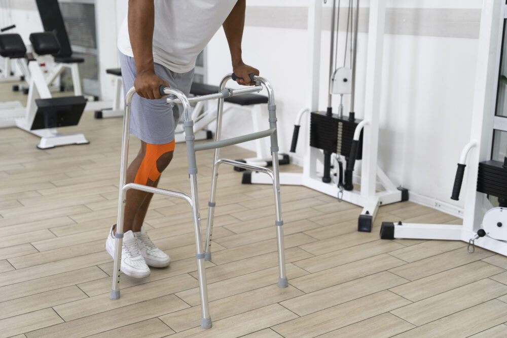 A person uses a walking frame in a gym, with strength‑training machines visible in the background.