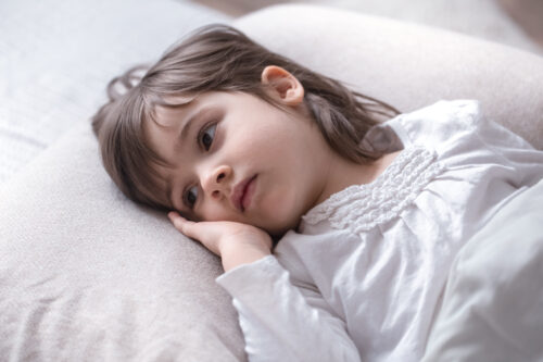 A child lies on a bed in a restless position, suggesting difficulty sleeping.