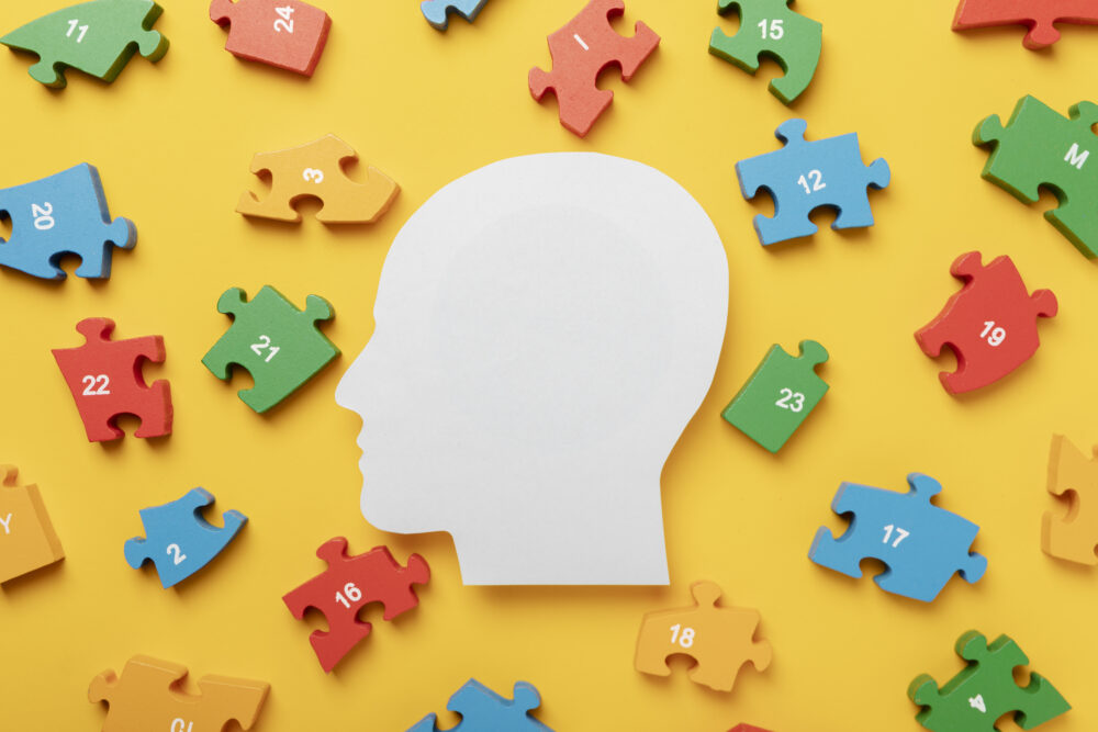 A white silhouette of a head is surrounded by colourful numbered puzzle pieces on a yellow background.