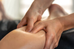 Hands apply firm thumb pressure to a person’s calf during a massage.