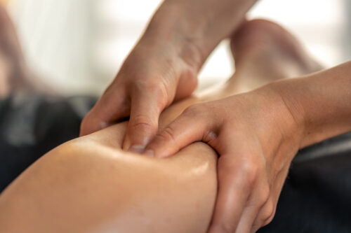Hands apply firm thumb pressure to a person’s calf during a massage.