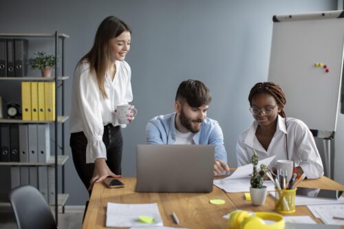Three adults collaborating at a desk with a laptop and documents.