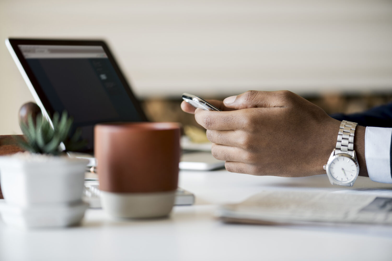 Person using a mobile phone at a desk with a laptop.